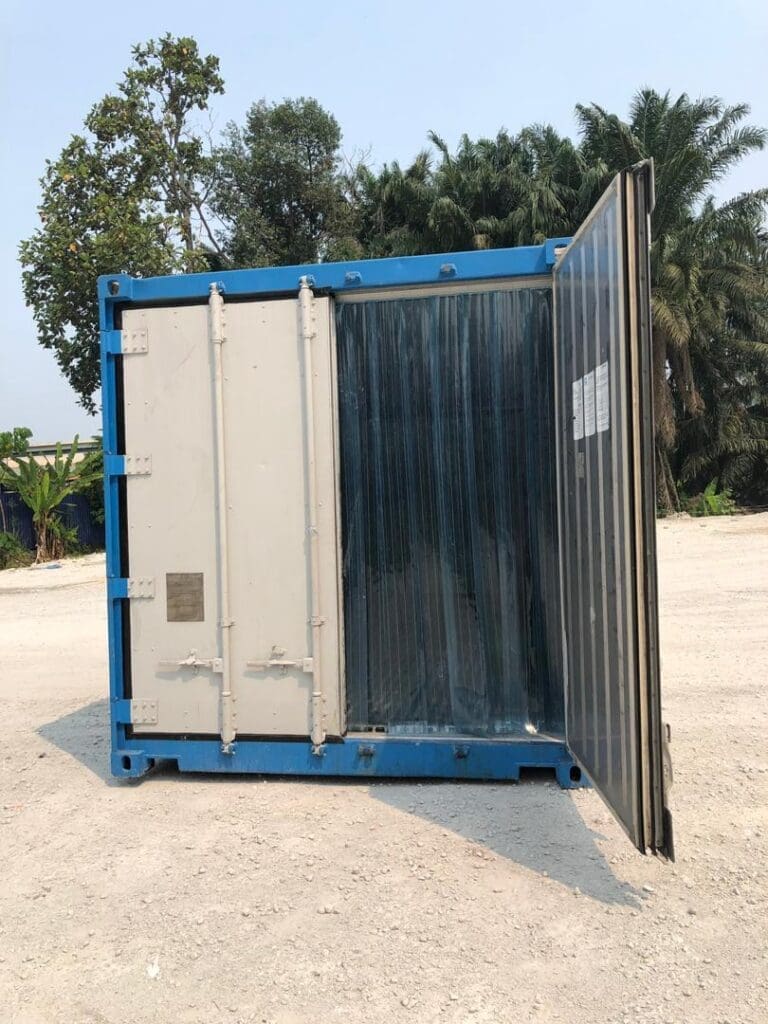 Blue and white shipping refrigerated container with its doors open, standing on a paved surface with greenery in the background.