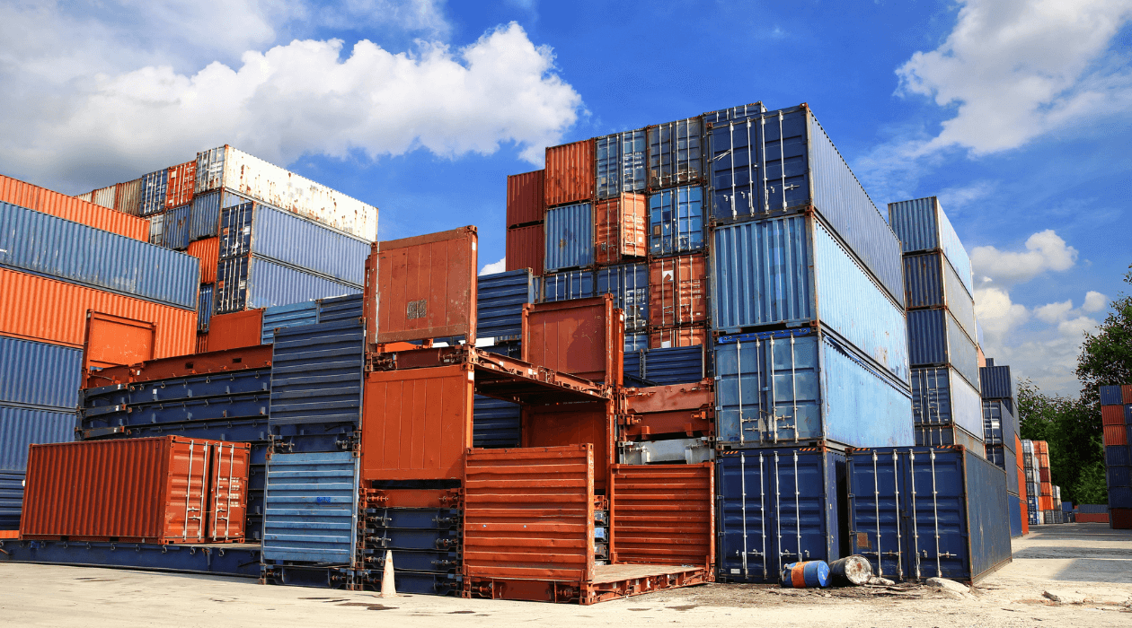 Stacks of colorful shipping containers at a freight terminal under a clear blue sky.